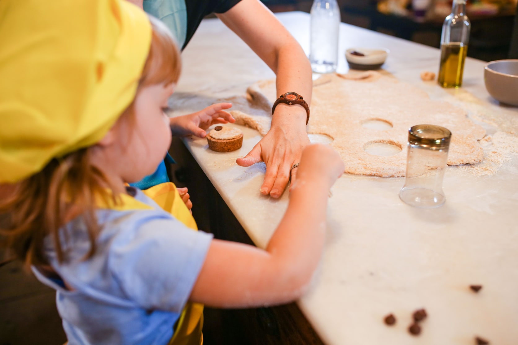 A young child in an apron cutting shapes from dough alongside a parent, illustrating how involving children in cooking supports development and wellbeing