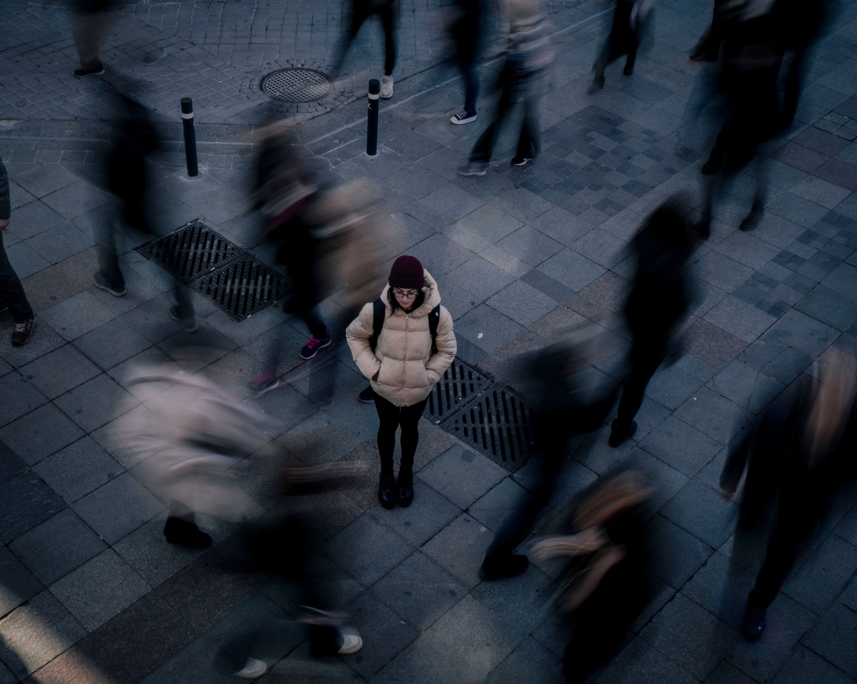 Alone in a crowd: what “growing isolation” means for our mental health A woman standing still and looking down in a busy city square while the crowd around her blurs into motion, illustrating the experience of feeling alone among other people