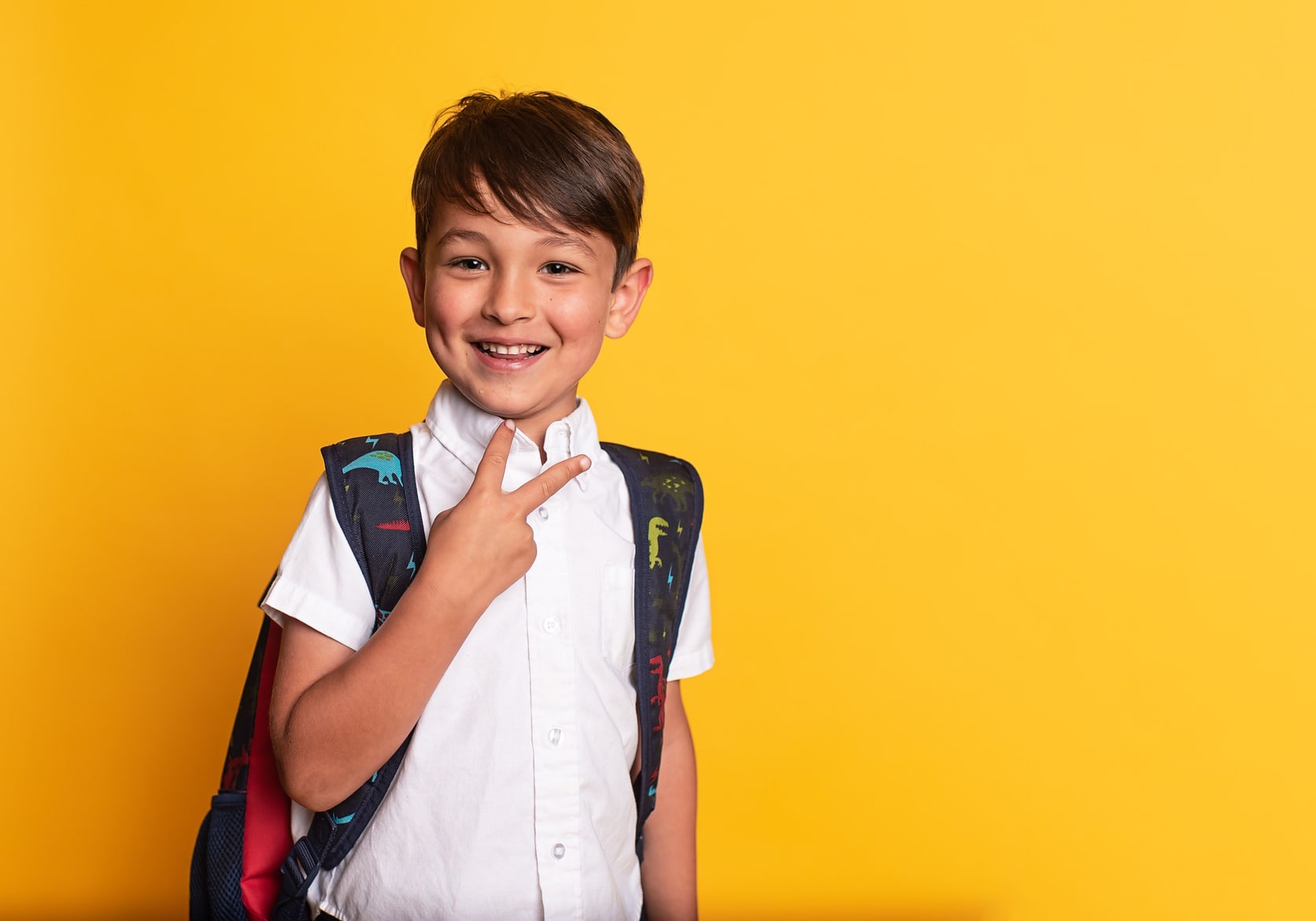 A smiling primary school child wearing a backpack against a bright yellow background, illustrating the return to school routine in September